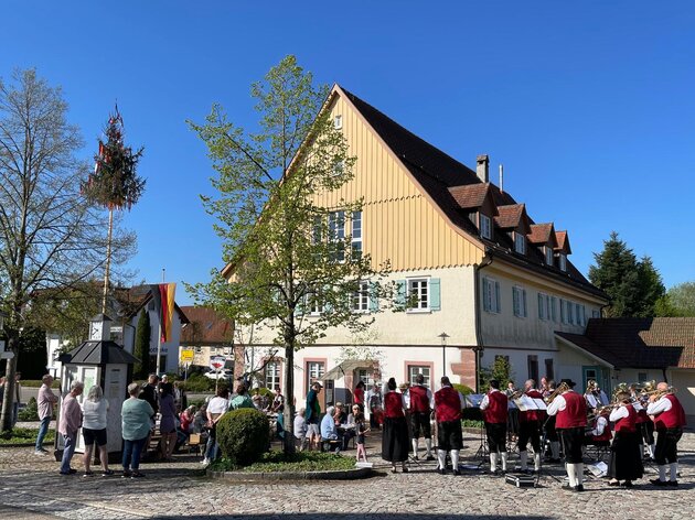 Der Musikverein spielt vor der historischen Fassade des Rathaus in Besenfeld. Am Bildrand ist der Maibaum mit seinen bunten Bändern zu sehen. 