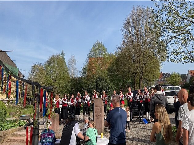 Menschen schauen dem Musikverein Besenfeld beim musizieren zu. Der Himmel ist blau und im Vordergrund ist ein historischer Brunnen. 