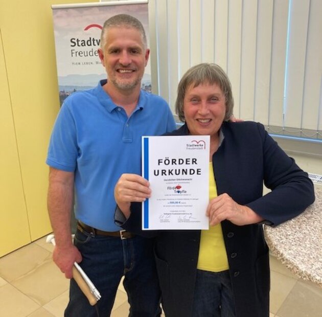 Petra und Torsten halten lächelnd eine Föderurkunde in die Kamera.
